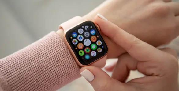 Novedades de Apple watchOS 26.2: Todo lo que debes saber antes de actualizar 85 Mujer interactuando con un Apple Watch dorado con correa rosa, mostrando la pantalla de inicio de watchOS con varias aplicaciones.