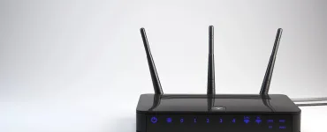 Router WiFi negro con tres antenas externas, LEDs indicadores de puertos LAN, USB y bandas 2.4G y 5G sobre fondo gris neutro