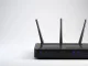 Router WiFi negro con tres antenas externas, LEDs indicadores de puertos LAN, USB y bandas 2.4G y 5G sobre fondo gris neutro