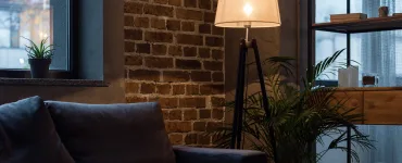Mito del standby: ¿Cuánto consumen tus bombillas inteligentes apagadas? 78 Lámpara de pie encendida en salón moderno con sofá gris y pared de ladrillo, ilustrando el uso típico de iluminación en hogares con bombillas inteligentes
