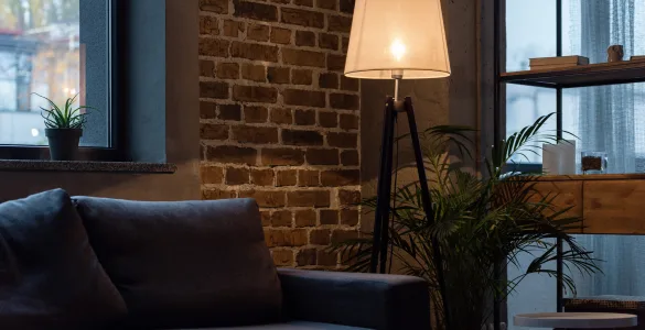 Mito del standby: ¿Cuánto consumen tus bombillas inteligentes apagadas? 84 Lámpara de pie encendida en salón moderno con sofá gris y pared de ladrillo, ilustrando el uso típico de iluminación en hogares con bombillas inteligentes