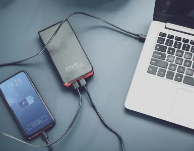 Cómo elegir un power bank: capacidad, vatios y USB-C para móvil y portátil 76 Power bank cargando dos móviles por USB-C junto a un portátil sobre la mesa