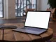 Portátil abierto con la pantalla en blanco sobre una mesa redonda de madera, junto a una libreta